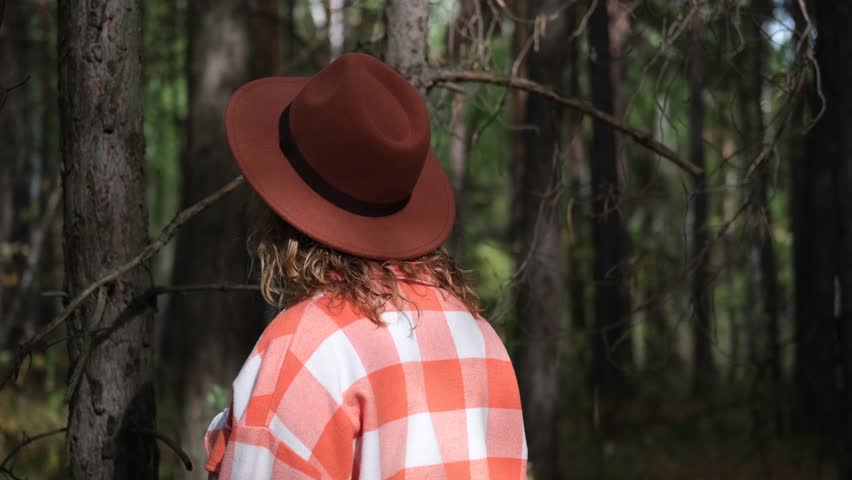 Portrait of a beautiful smiling woman in a brown hat walks with pleasure in the autumn forest. The woman breathes clean air.