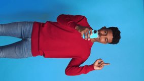 Cheerful black boy with smartphone pointing with a finger. Vertical video.