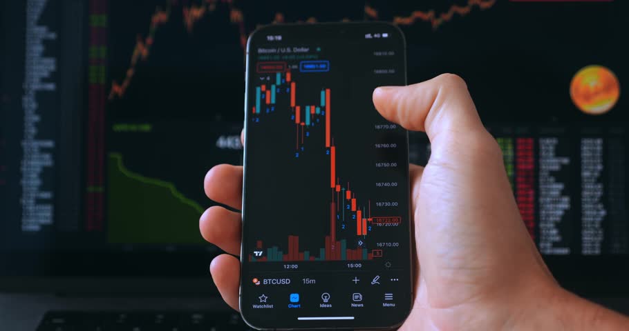 Male investor working with mobile phone on crypto stock exchange in front of stock market financial screen. Trader analyzing stock market investments on mobile phone application. Crypto currency | Shutterstock HD Video #1099078917