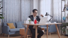 Sick Asian Businessman Holding A Thermometer To The Video Call With Doctor On A Laptop While Working At Home
