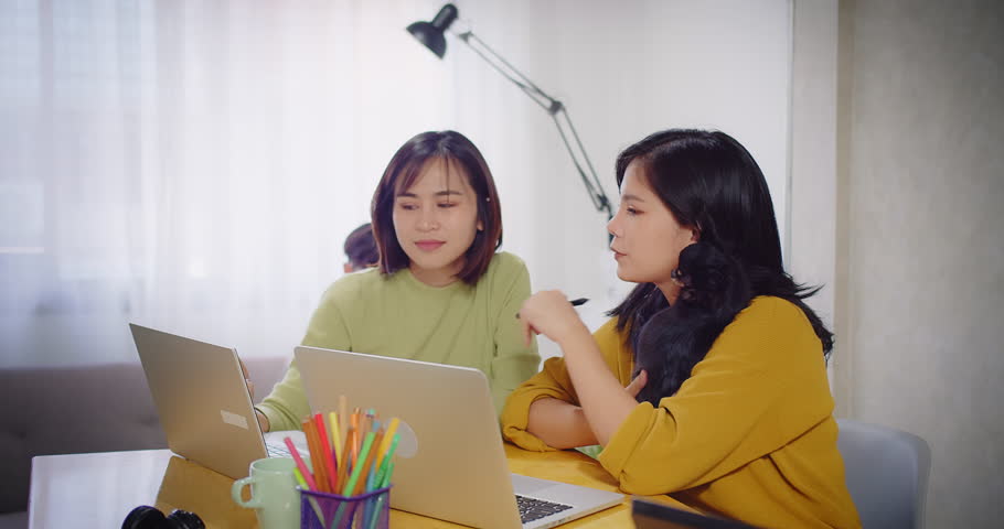Two of Asian young creative women in smart casual discussing explaining online job having teamwork at their desks and working on laptops working at home office, coworker business concept | Shutterstock HD Video #1099084263