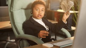 Portrait of cute little businessman kid child support manager with wireless headset hold stack of money dollars talking by online meeting conference video call using webcam computer at workplace
