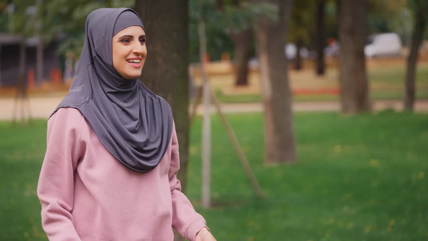 Joyful muslim female in hijab catching and throwing flying disc, resting in park