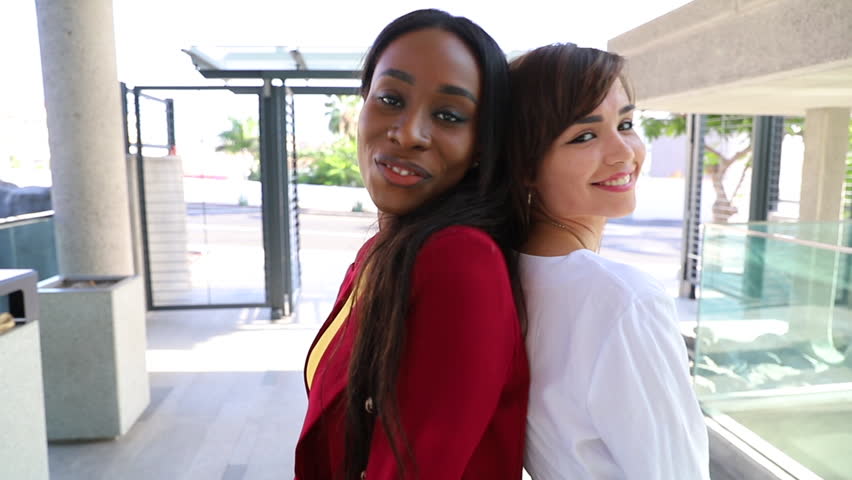 Two smiling businesswomen of different ethnic backgrounds pose back to back