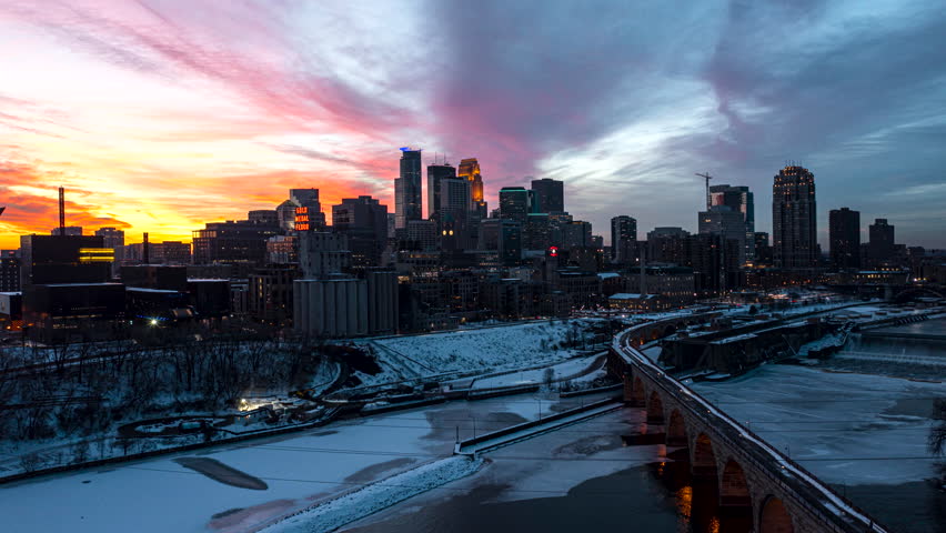 Aerial hyperlapse of the sun setting behind the Minneapolis skyline with snow covering the ground.