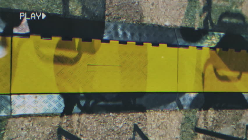 Old VHS tape effect: a man carefully walking on a yellow strip on the floor, indicating a safe path into a dangerous place.
