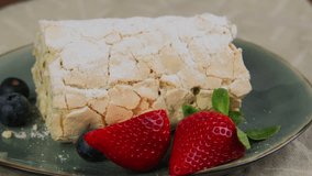 Meringue roll cake with cream and fresh strawberry and blueberry. Meringue roulade sprinkled with sugar powder, summer dessert served on plate, rotation video. High quality 4k footage