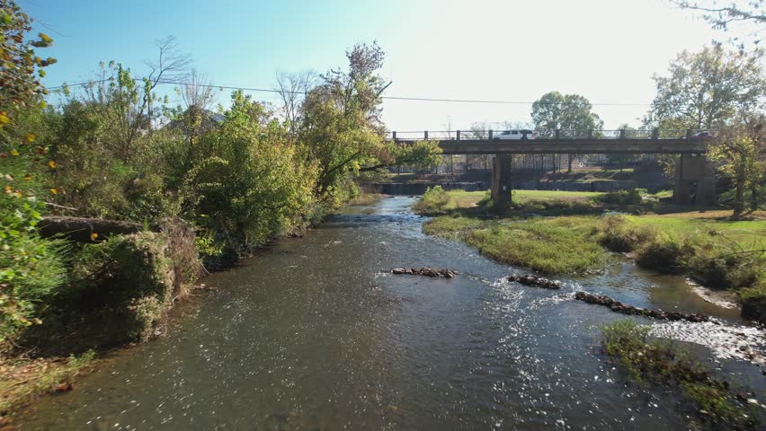 Aerial pass under bridge following creek approaching waterfall in Old Town Helena, Alabama