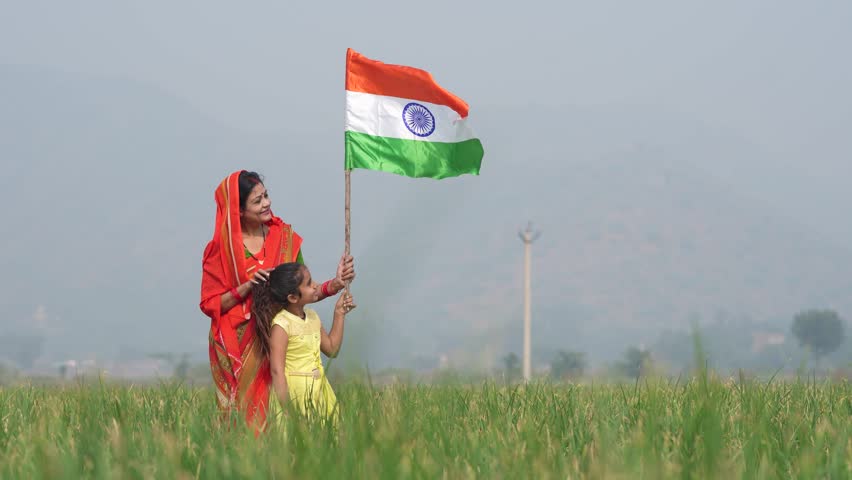 Indian rural woman and her little daughter waving national tricolor flag at agriculture field.