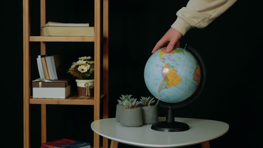 Globe on the table. The hand turns the earth. Point to the map