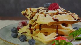Soft Belgian waffles sprinkled with sugar powder, served with cream topping and fresh berries, a pile of fluffy waffles, sweet dessert for breakfast, slow motion rotation video clip, 4k footage