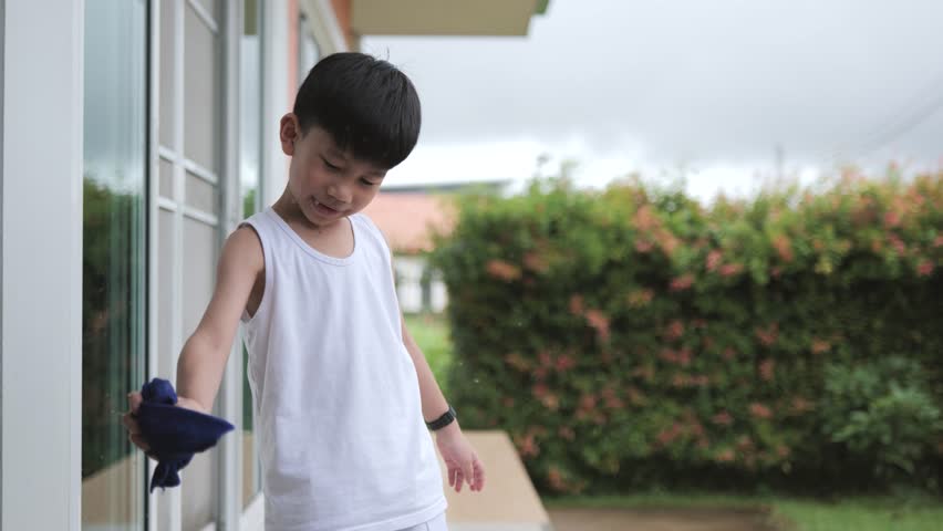 Asian boy spins a wet blue fiber cloth to rinse the water while cleaning the house.