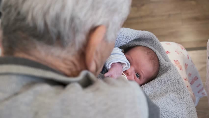 grandpa with baby. Baby on grandfather's lap. newborn infant looking up at the camera. old man holding baby with pacifier. infant looking up with huge beautiful eyes. soft little baby. life concept.  Royalty-Free Stock Footage #1099116323