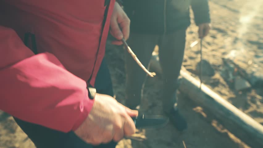 Male hands make a sharp stick out of a branch with a knife. A tourist with a knife makes pegs from wooden sticks, skewers for sausages. Craft wooden skewer