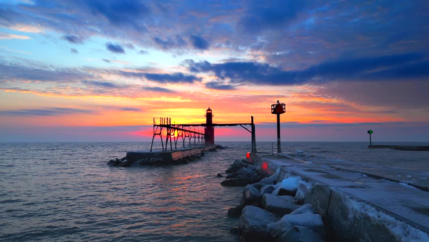 Iconic Lighthouse beacon silhouetted against fiery Lake Michigan twilight horizon, moving aerial view.