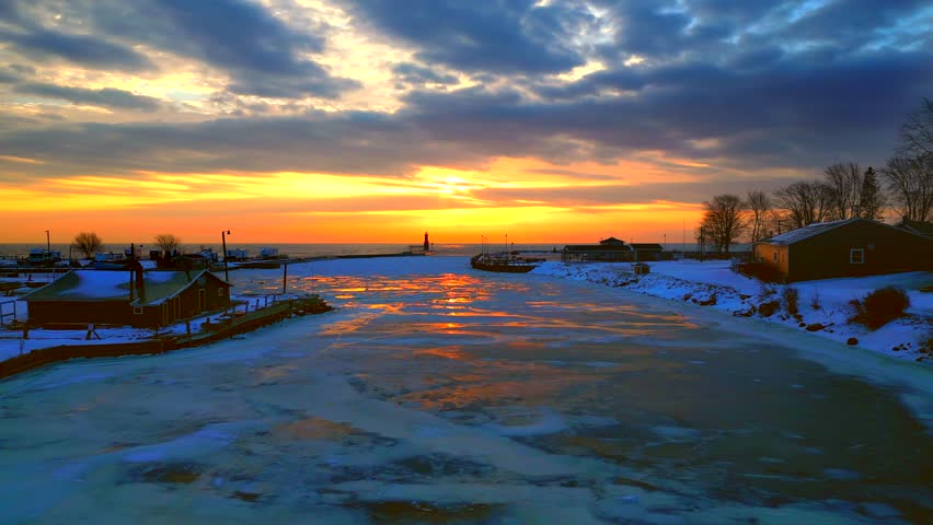 Fiery Lake Michigan dawn over Cracked harbor ice moving with currents, aerial view.
