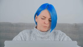 Blue haired millennial woman works on laptop computer at home. Young Ukrainian female person with dyed hair studying online with notebook pc