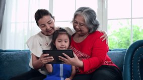 Mother and grandma teaching child with tablet to do their homework at home, Asian happy family education concept
