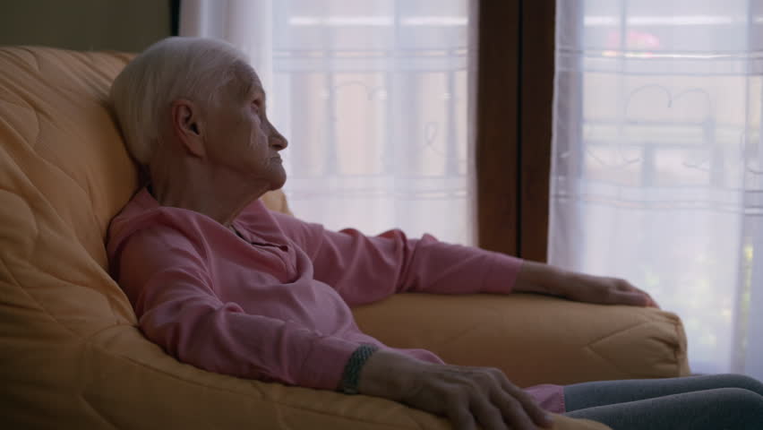 Carefree relaxed old woman thinking looking at camera and looking away sitting indoors. Side view senior Caucasian retiree thinking resting at home sitting in cozy armchair | Shutterstock HD Video #1099123245