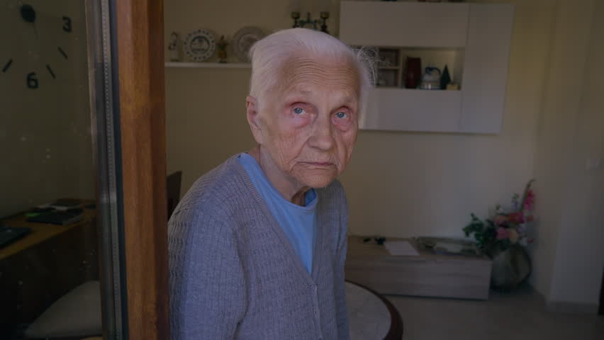 Grey-haired old Caucasian woman looking away smiling standing at home indoors. Portrait of positive senior female retiree in room | Shutterstock HD Video #1099123265