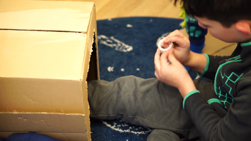 A boy sitting on the floor and using patches for a carton box