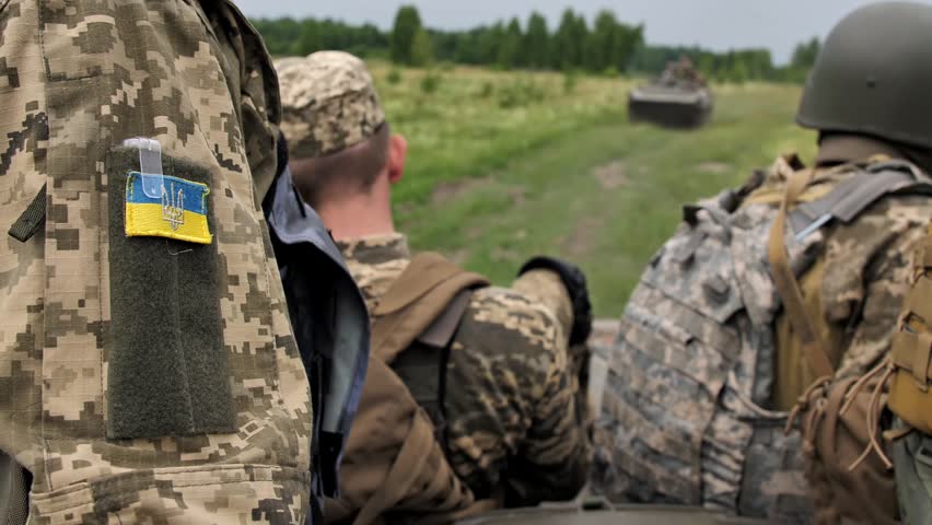 Military personnel of Armed Forces of Ukraine ride on roof of an armored personnel carrier or armored infantry vehicle. Close-up of patch flag of Ukraine on shoulder of soldier. War in Ukraine Royalty-Free Stock Footage #1099135057