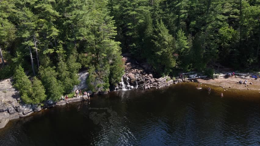 An aerial of people on granite rocks swimming and jumping in the water at High Falls Park, Muskoka, Canada