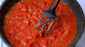 Hot boiling tomato sauce being stirred in pan with fork, red tomato sauce simmering on kitchen stove, top view video, 4k video clip