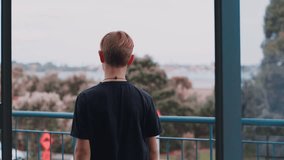 Portrait video of a young kid with coloured hair walking up to the balcony. His hair is multi-coloured and the scene is dark cinematic and eerie.