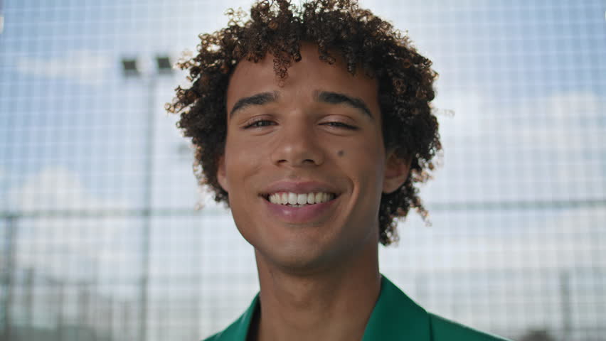 Positive teenager laughing street fashion portrait. Smiling young man standing looking camera alone closeup. Curly hair model demonstrating emotions at stadium. Cheerful guy face enjoying outdoors Royalty-Free Stock Footage #1099143095