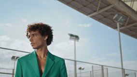 Curly student looking camera at stadium background fashion portrait. Serious model posing alone in trendy clothes. Stylish hair guy showing individuality closeup. Modern teen face relaxing outdoors - Powered by Shutterstock - Get 15% off with code: PIKWIZARD15