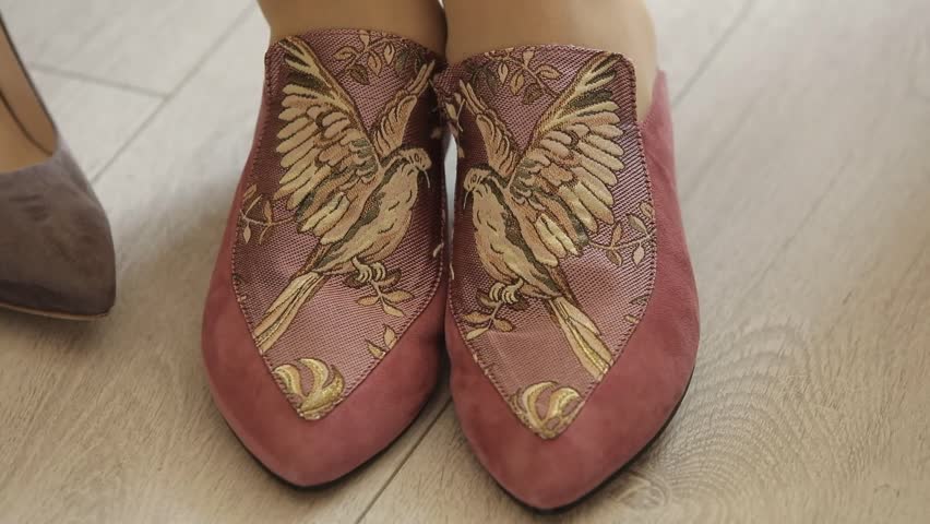 a woman tries on beautiful sandals made of red leather with satin stitch decor, a golden bird with wide-spread wings on a branch