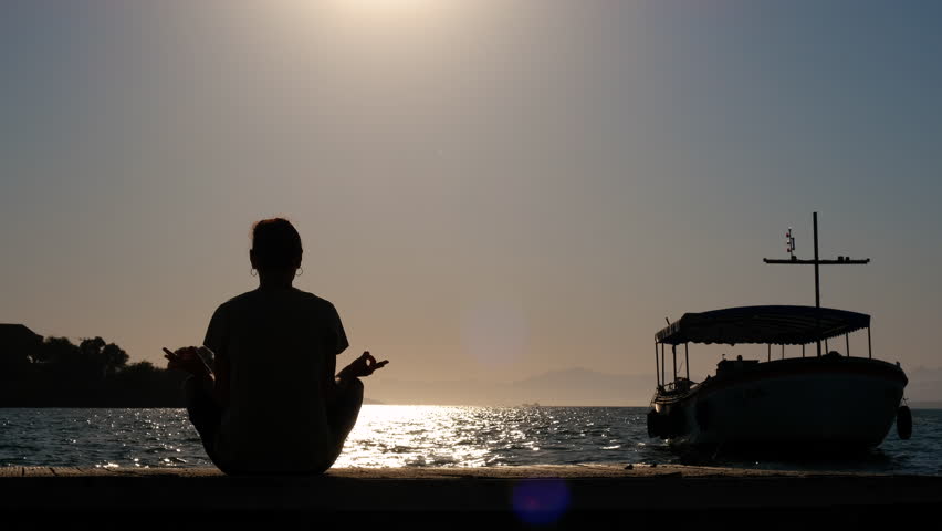 Silhouette of an older woman on the seashore at sunset against the backdrop of boats. Meditation for mental health.