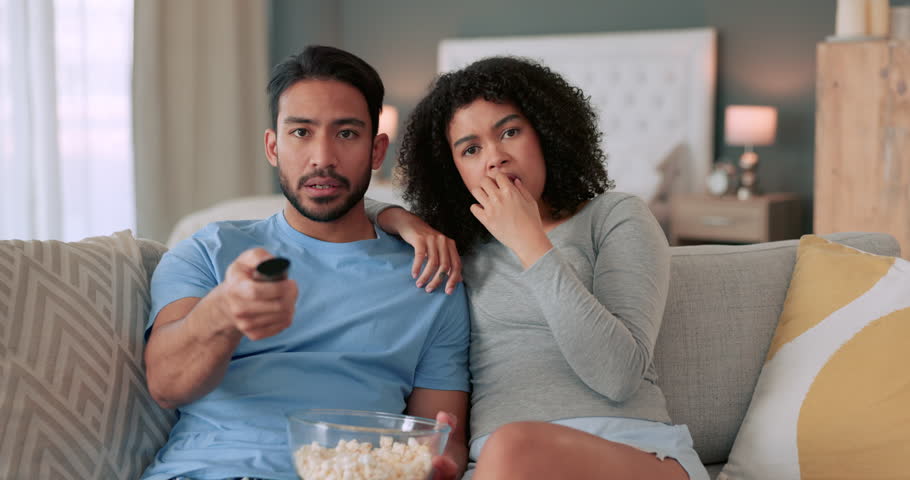 Arguing couple, tv remote and controlling woman changing the channel to watch a movie and eat popcorn on the sofa at home. Fighting, angry and upset man watching sports while girlfriend grabs control
