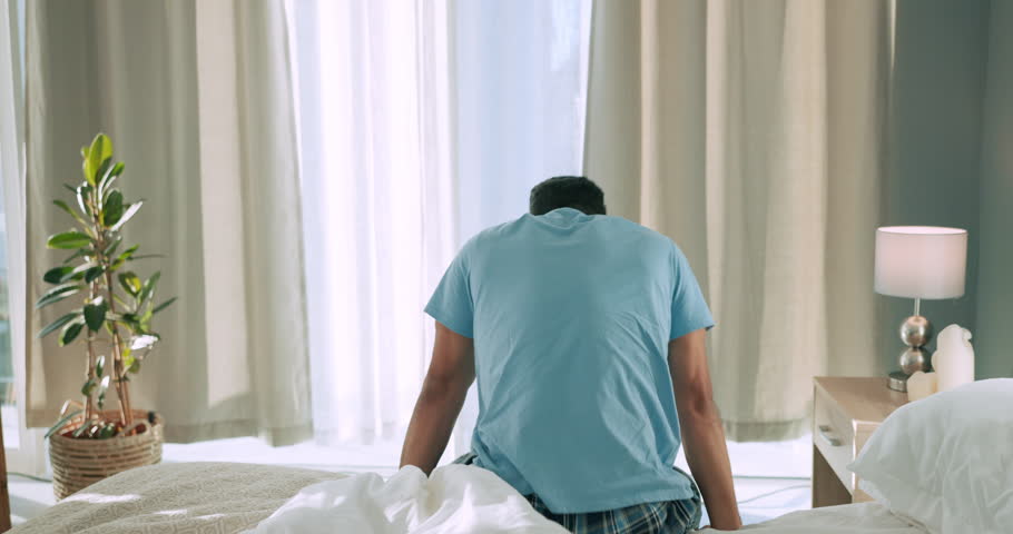 Wake up, sunrise and man stretching in his bedroom looking at sunlight through curtains in the morning. Mindset, lifestyle and back view of a young person ready to start day after sleeping at home Royalty-Free Stock Footage #1099148013