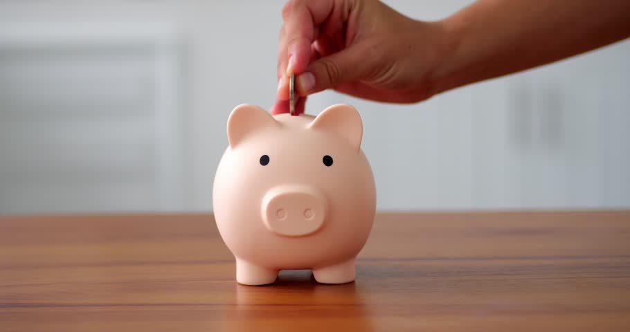 save money for vacation. A piglet is standing on a wooden table and an unrecognizable hand is save money by throwing money into a piggy bank. View from the side save money Royalty-Free Stock Footage #1099148599