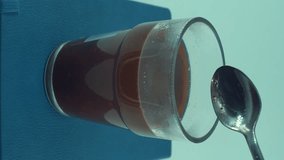 A vertical close up shot of a glass of black coffee stirring, man hand wih a silver spoon, floating cafe grains, studio light, 4K video