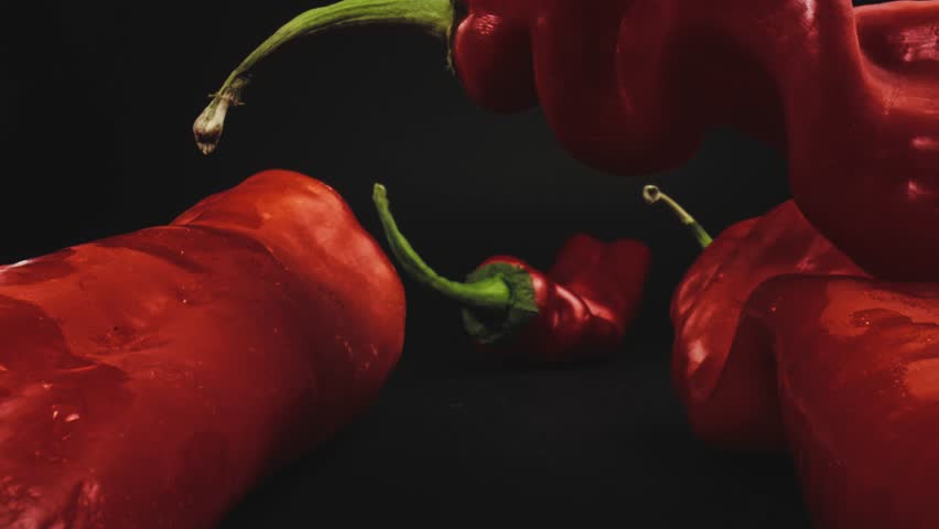 Four fresh red hot peppers. The camera passes in between. Dolly shot with macro probe lens. Slider movement.