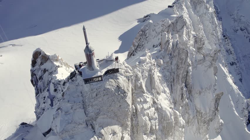 Observatory and antenna summit of Aiguille du Midi near Mont Blanc Mountain peak with visitor center below, Aerial dolly up looking down shot