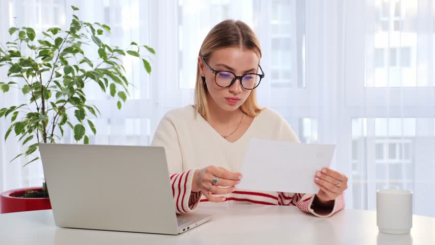 Sad shocked woman girl sitting on couch at home reads received bad news holds documents paper letter feels desperate about eviction not passing the exam, domestic bills or debt, college expulsion. | Shutterstock HD Video #1099154579