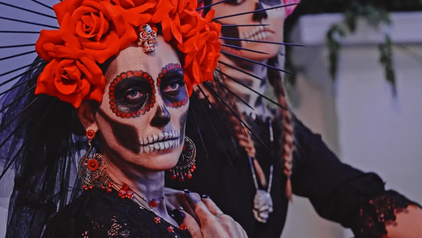 Close-up slow motion. Two Women with sugar skull make-up and costumes sit on the steps