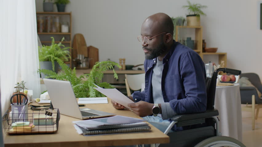 African American man in wheelchair discussing business paper via online video call on laptop while working remotely from home | Shutterstock HD Video #1099157593