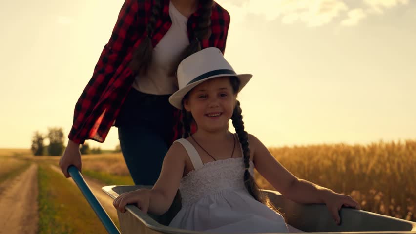 Two little sisters play in a field at sunset. Children ride on a garden cart. The kids are happy. A little girl sits in a cart and laughs. Happy family.