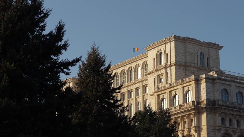 Flag of Romania on the Palace of the Parliament (Casa Poporului in Romanian language). 4K video with the waving flag against blue sky background in Bucharest.