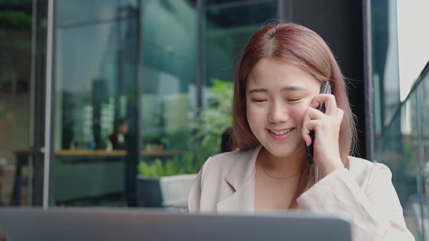 Smiling young business woman talking on phone and using laptop for working at modern office | Shutterstock HD Video #1099159361