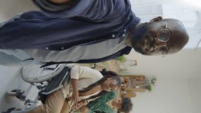 POV vertical shot of joyous African American man, his wife in wheelchair and little son smiling and chatting on camera while video calling or filming vlog at home