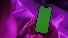 Back view of woman holding chroma key green screen smartphone watching content without touching or swiping.