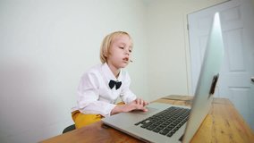 A preschooler in white shirt and black tie bow has a video call with his online teacher. Online lesson at home for a 5 years old caucasian boy. Remote education concept