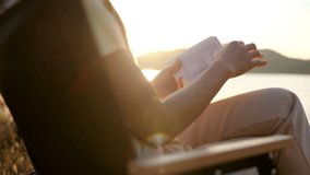 Video footage of Close up of woman is reading a book in meadow with mountain float on dam and sunset sky view.