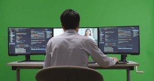 Back View Of Asian Man Developer Having Video While Write Code With Multiple Computer Screens In Green Screen Studio
